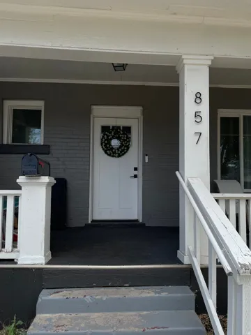 Front porch featuring a white entry door with frosted glass paneling, a dark grey painted brick facade, white trim, and white porch columns
