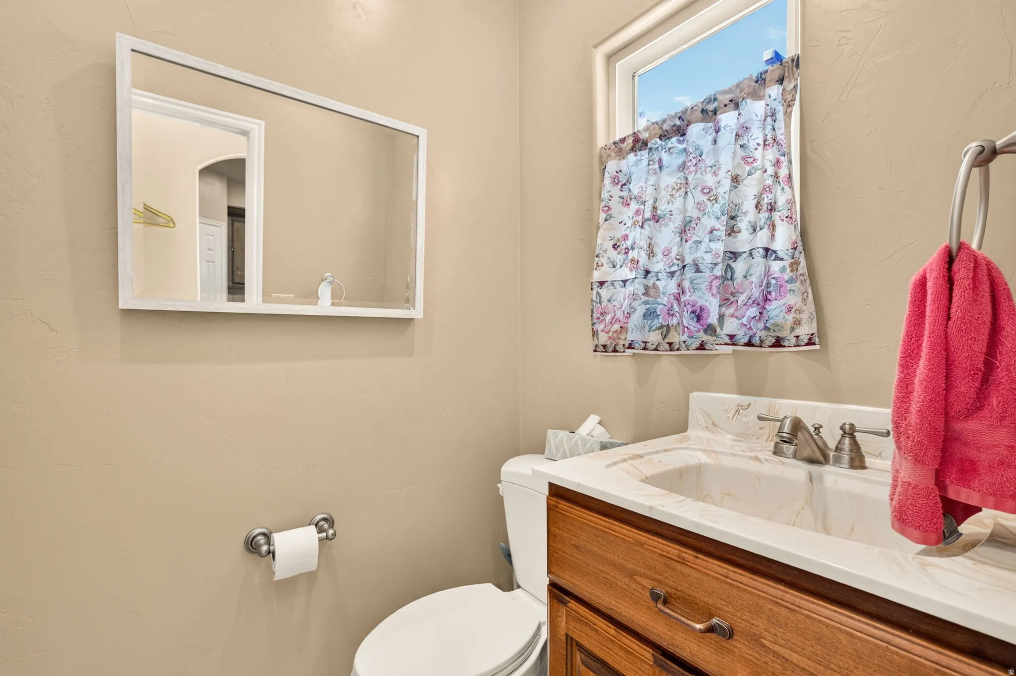 Bathroom featuring a wood-finish vanity with a built-in sink, a white-framed mirror, and a window