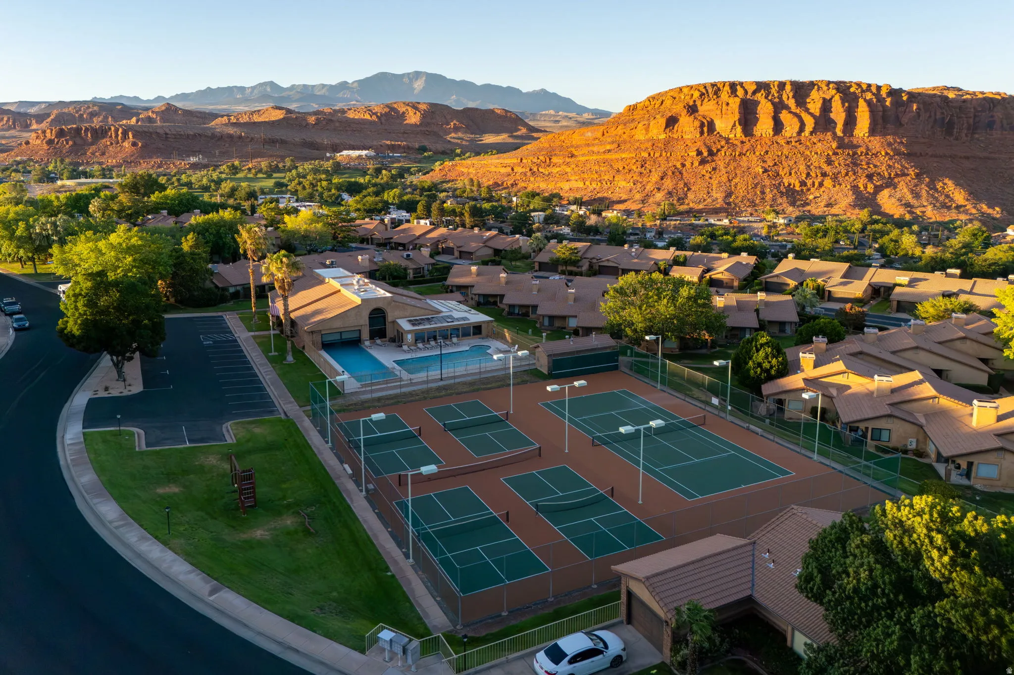 Community amenities featuring multiple tennis courts, a central clubhouse, and an outdoor swimming pool, all surrounded by residential properties and natural desert landscape