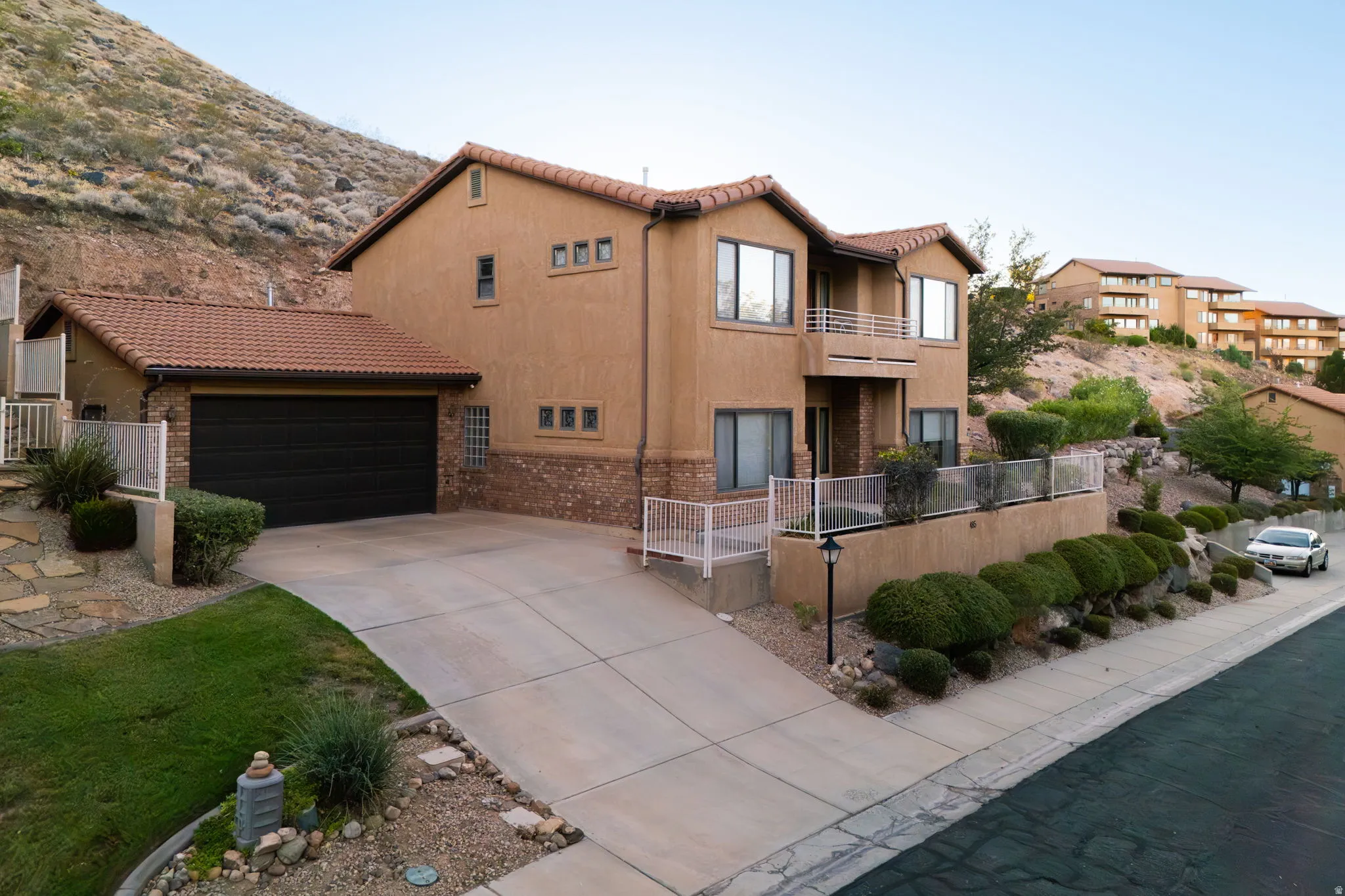 Terracotta tile roof and stucco exterior featuring brick accents, an integrated garage, a paved driveway, and multiple balconies with white railings