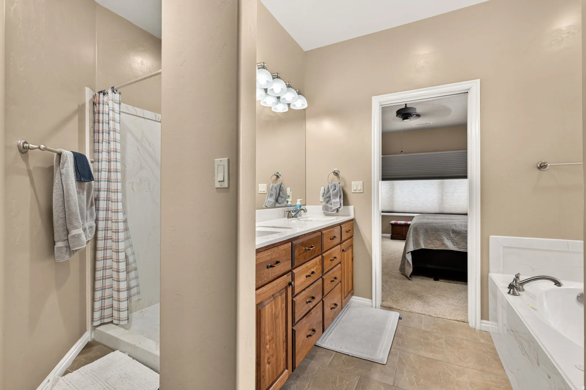 Bathroom featuring a dual vanity with wood cabinetry, a built-in bathtub with a white surround, a shower with a white tile enclosure, and tiled flooring