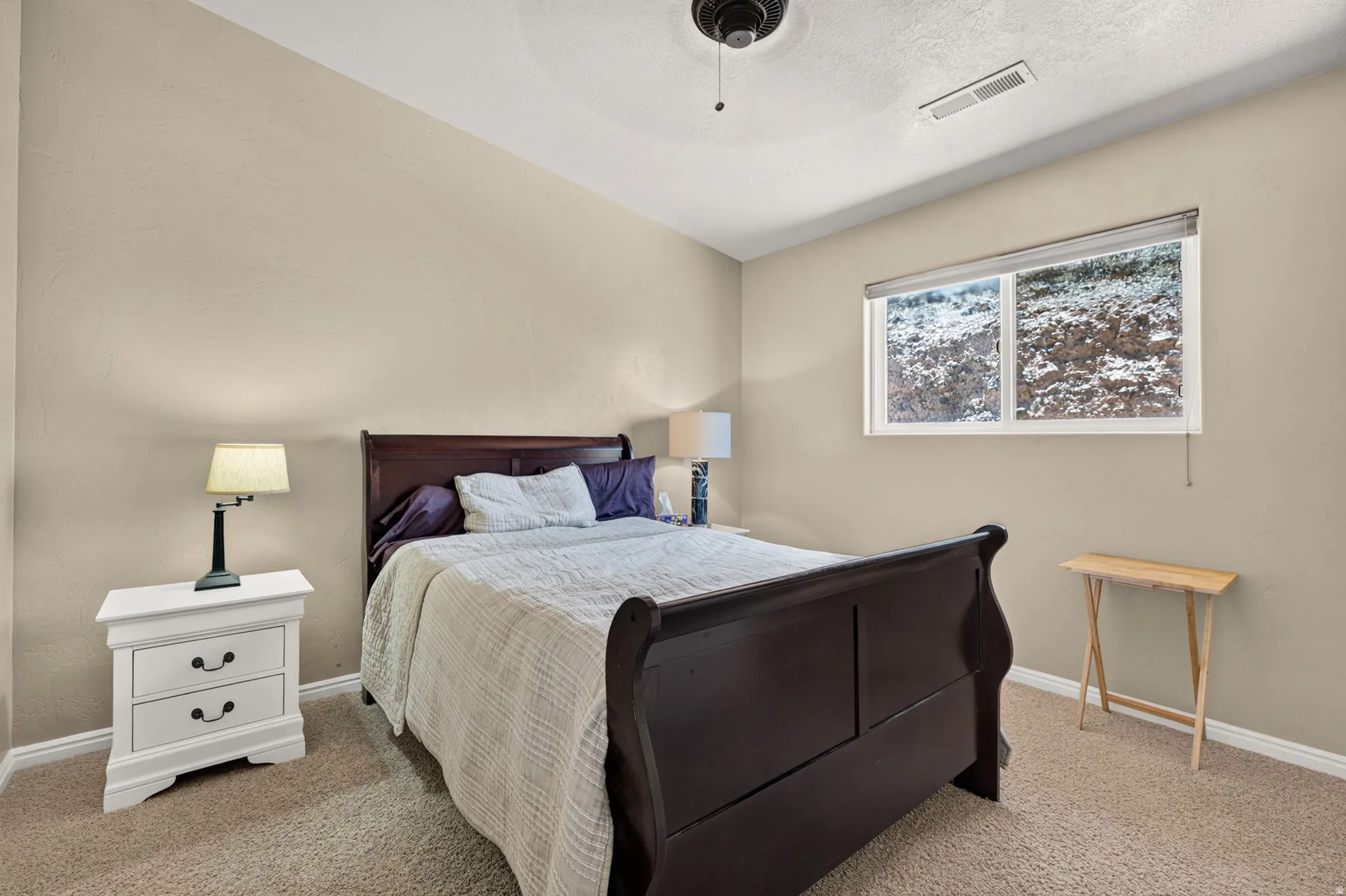 Carpeted room featuring neutral-toned walls, a single window with a roller shade, and a ceiling-mounted fan fixture