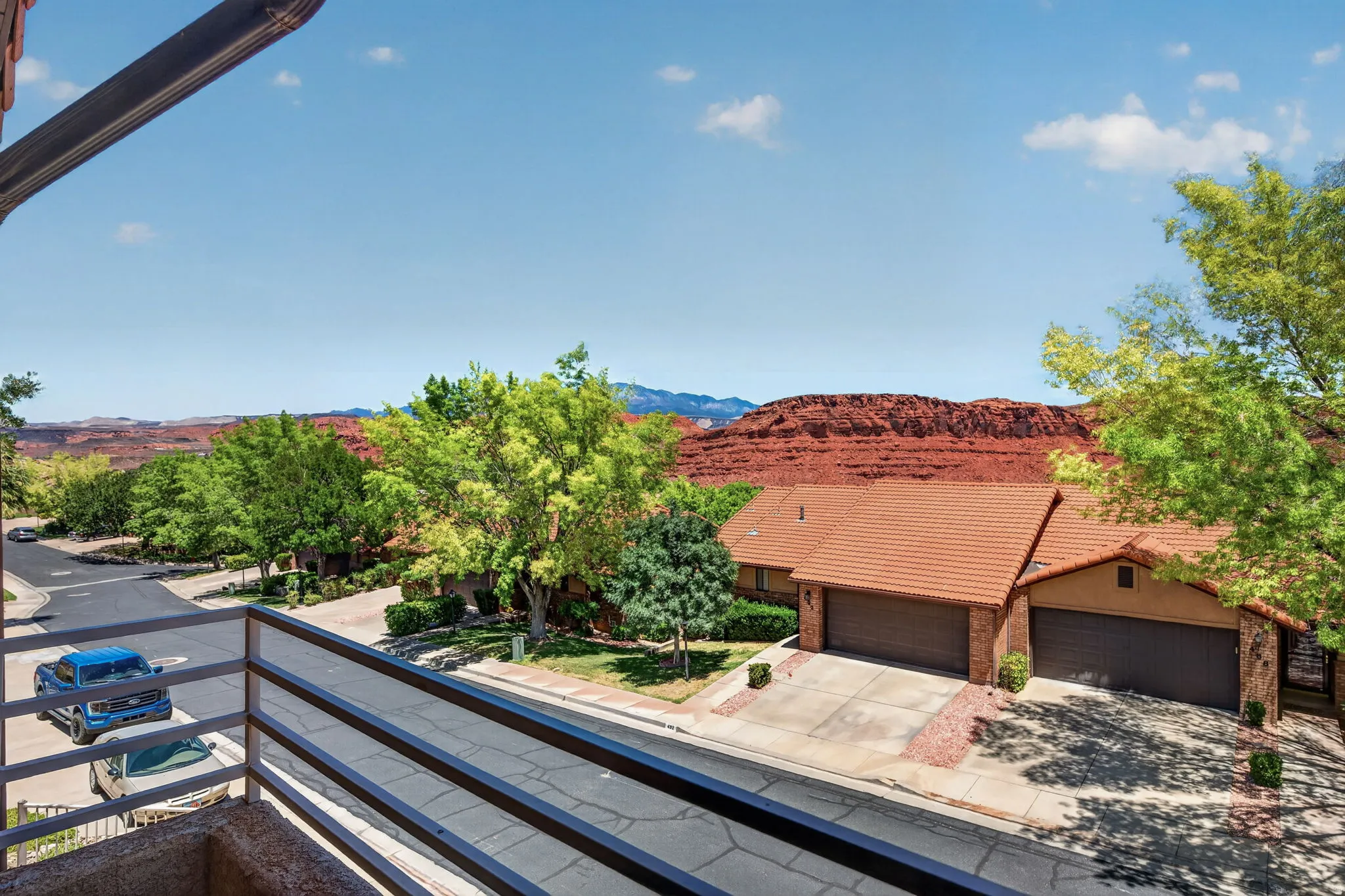 Red rock landscape backdrop with multiple dwellings featuring terracotta roof tiles, attached garages, and mature greenery