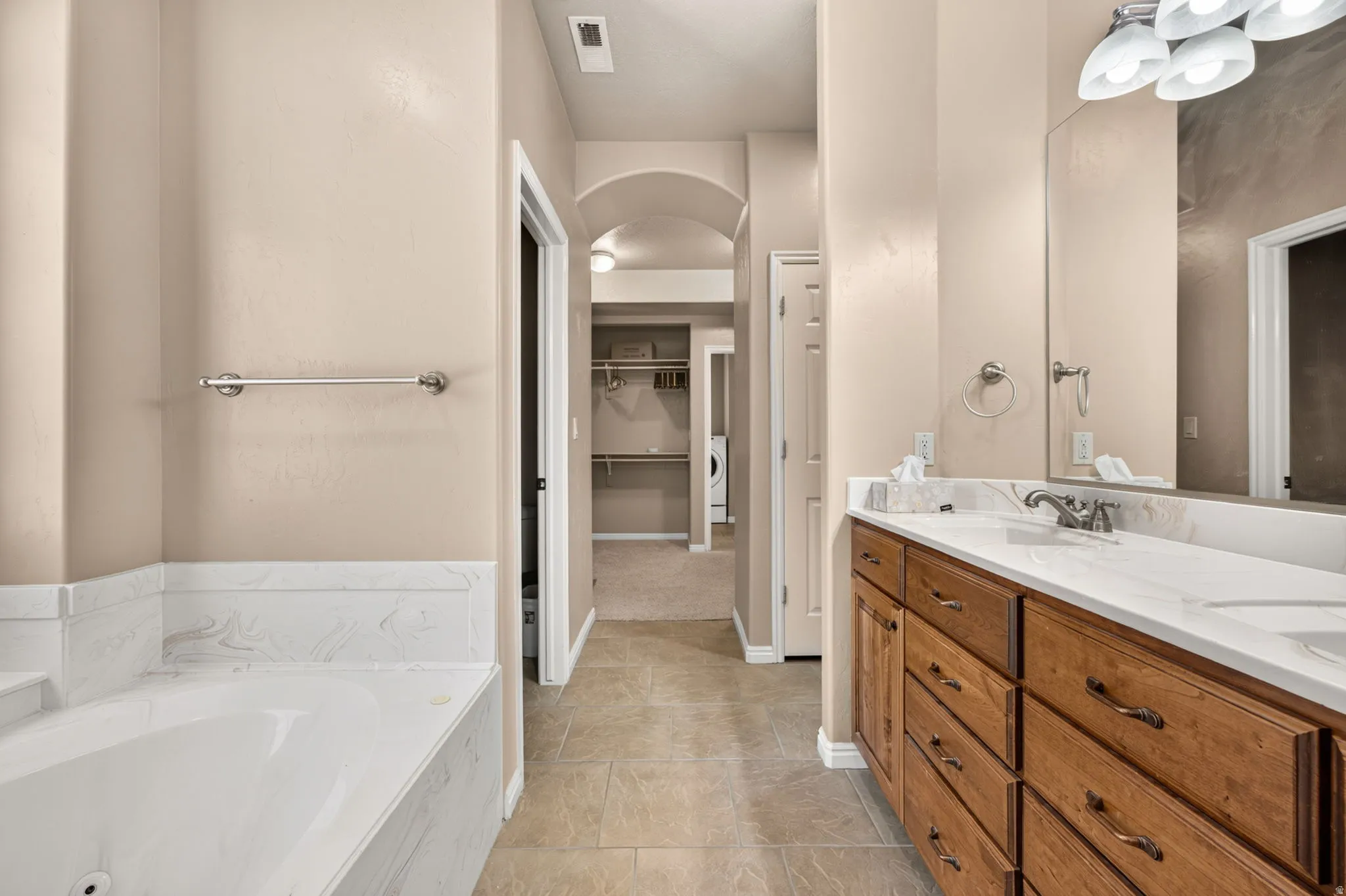 Bathroom featuring a dual vanity with a white countertop and wood-finish cabinetry, a built-in tub with white surround, and tile flooring