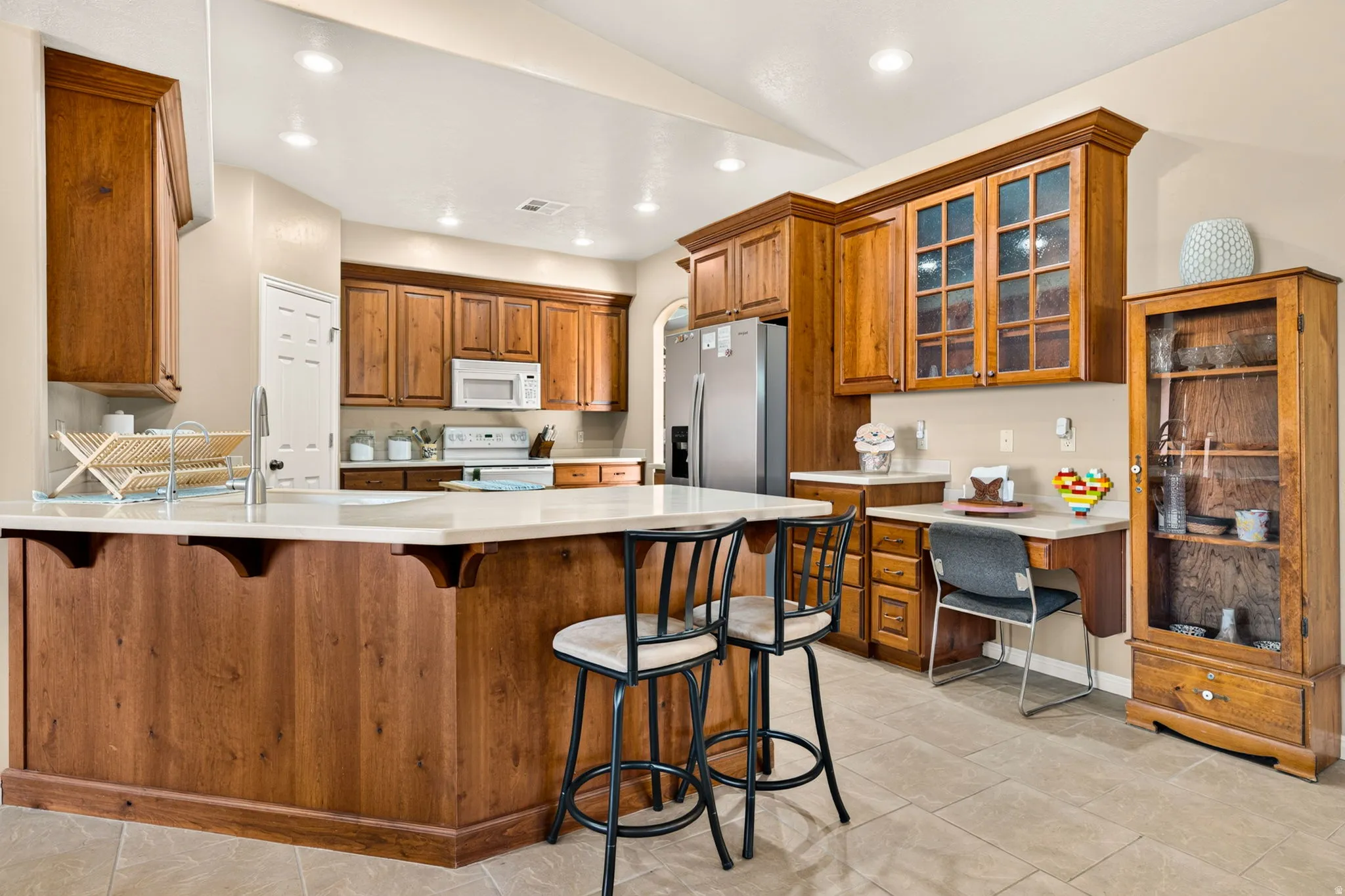 Kitchen featuring wood-finish cabinetry, stainless steel appliances, a center island with countertop seating, recessed lighting, and tile flooring