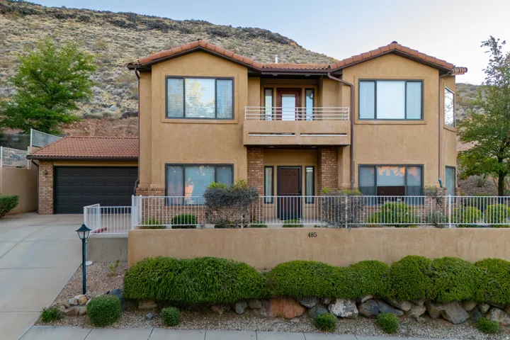 Terracotta tile roofline over a stucco exterior, featuring a two-car garage, upper-level balcony, and an elevated front entrance with a decorative security fence