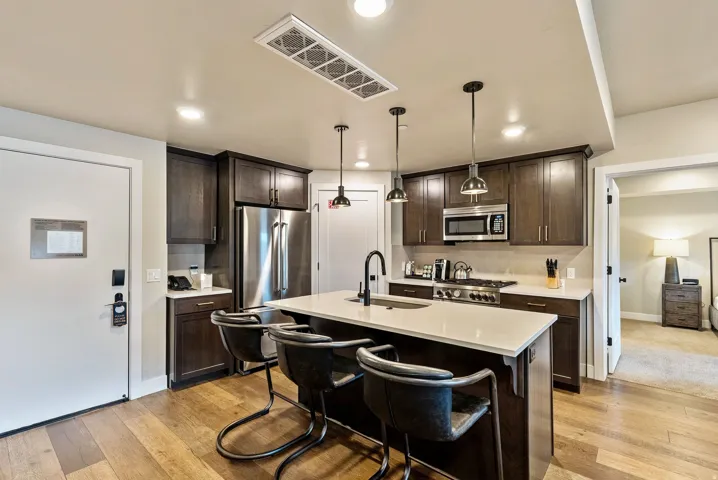 Modern kitchen featuring wood-finish flooring, dark wood cabinetry, stainless steel appliances, a center island with seating, and pendant lighting