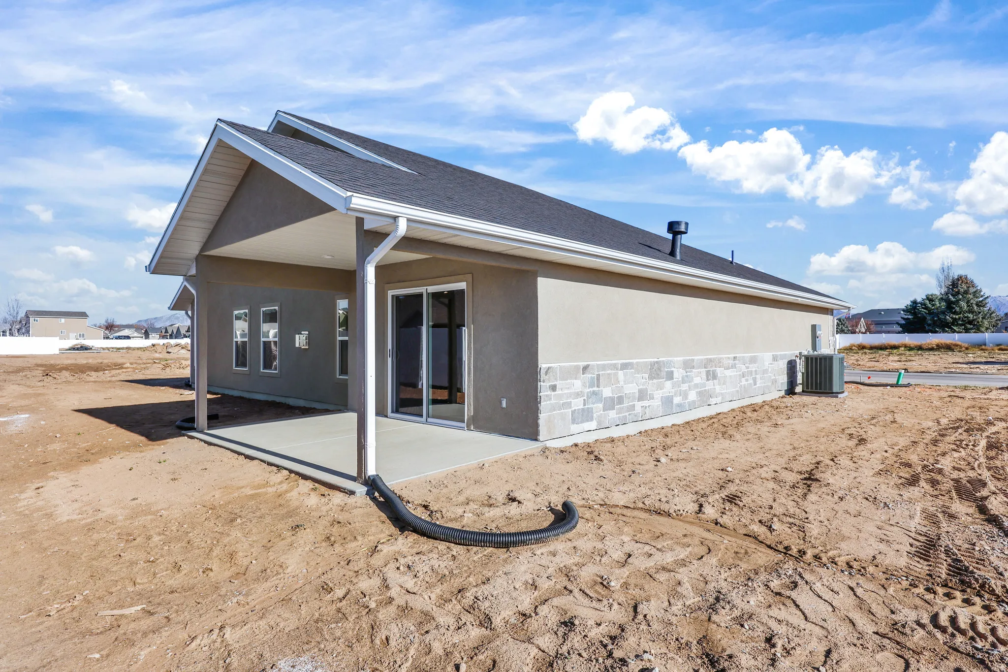Rear exterior featuring a covered concrete patio, sliding glass doors, and multiple windows