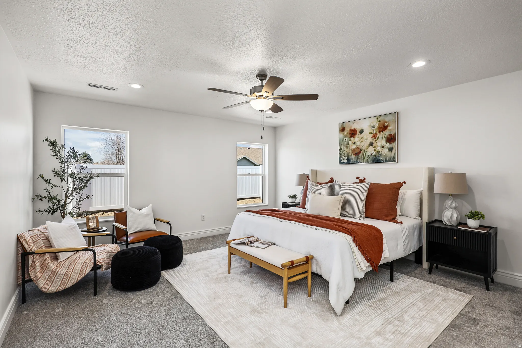 Spacious bedroom featuring light gray carpeting, crisp white walls, multiple windows providing natural light, a ceiling fan with integrated lighting, and recessed ceiling lights