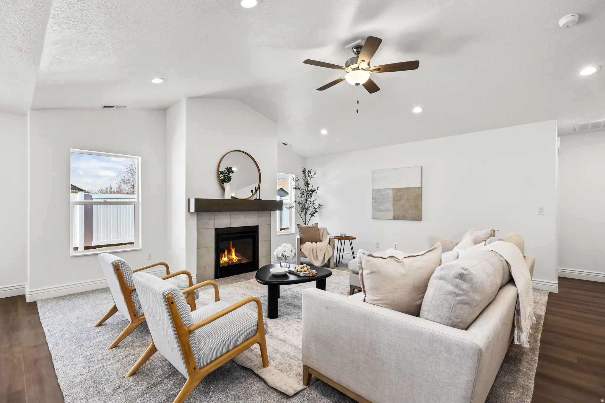 Living area featuring a floor-to-ceiling tiled fireplace with a wood mantel, vaulted ceiling, recessed lighting, ceiling fan, and wood-finish flooring