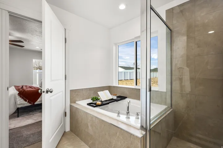 Bathroom featuring a built-in soaking tub with deck-mounted fixtures, a glass-enclosed shower with full-height tile, and a large window providing natural light