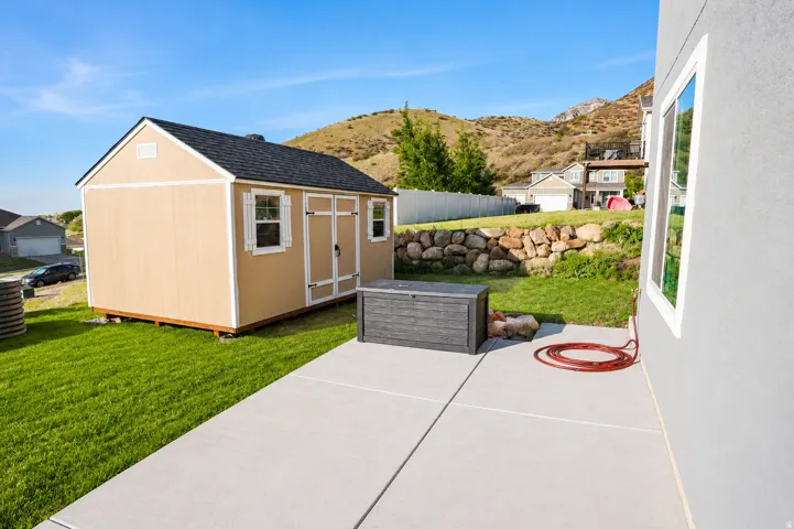 Rear yard featuring a concrete patio, a detached shed with a black shingle roof and double doors, and a rock retaining wall