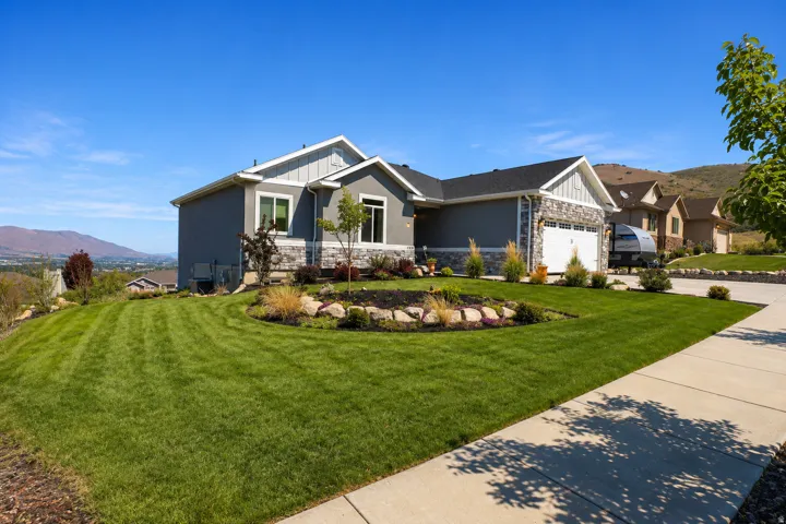 Contemporary exterior featuring a two-car garage, stone and siding accents, and a landscaped front yard with established plantings
