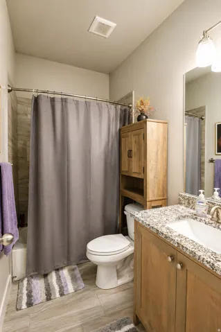Bathroom featuring a full tub with tiled surround, wood-finish flooring, a vanity with granite countertop and undermount sink, and a wooden storage cabinet