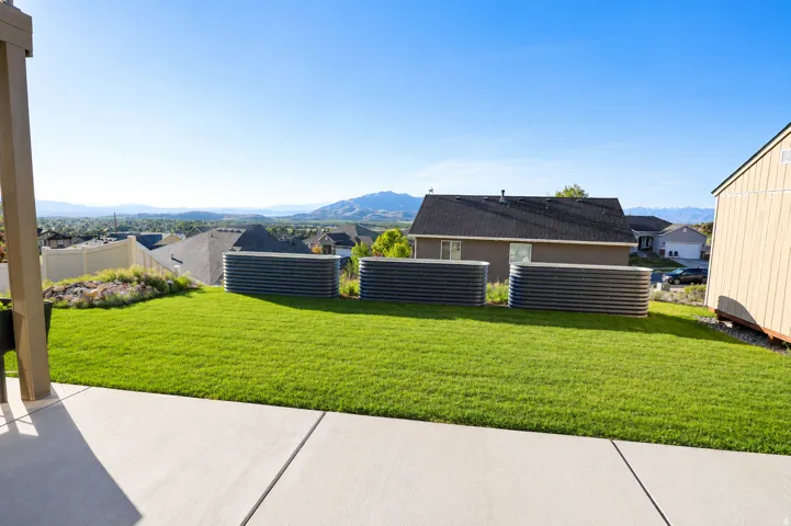 Expansive green lawn with mountain backdrop, concrete patio, and three large raised garden beds