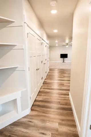 Hallway featuring wood-finish flooring, recessed lighting, and built-in storage with white paneled doors