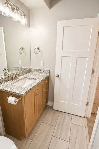 Bathroom vanity featuring a light wood-finish cabinet with brushed nickel hardware, a granite countertop with an integrated sink, and an overhead three-bulb vanity light fixture