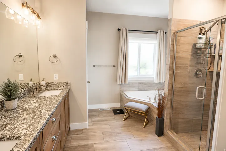Bathroom featuring a corner soaking tub, a glass-enclosed shower with tile surround, a double vanity with stone countertop, and wood-finish flooring