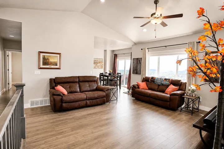 Spacious living area featuring vaulted ceilings, recessed lighting, wood-finish flooring, a ceiling fan with light fixture, and large windows
