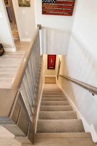 Carpeted staircase featuring a light wood-finish handrail and banister