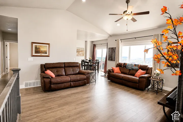 Spacious living area featuring vaulted ceilings, recessed lighting, wood-finish flooring, a ceiling fan with light fixture, and large windows