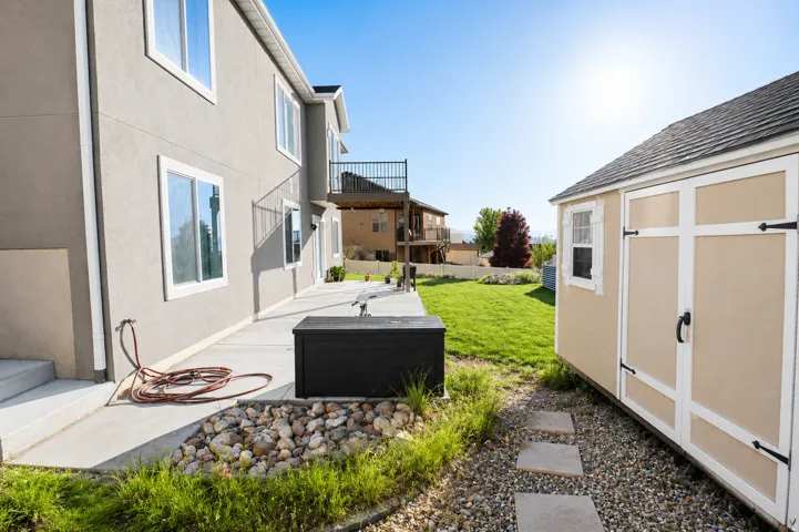 Spacious backyard featuring a detached storage shed, concrete patio, and upper-level balcony