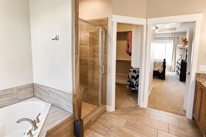 Bathroom featuring a soaking tub with brushed nickel fixtures, a glass-enclosed shower with tile surround, wood-finish flooring, and a vanity with a granite-look countertop