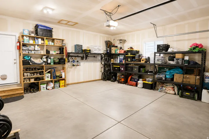 Spacious garage featuring concrete flooring, unpainted drywall, overhead lighting, an entry door with steps, and a window with blinds