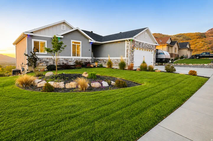 Contemporary exterior featuring a stone and stucco facade, an attached garage, landscaped front yard with rock accents, and a concrete driveway