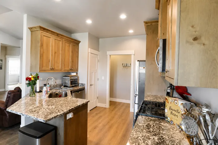 Bright kitchen featuring light wood cabinetry, stone-finish countertops, stainless steel appliances, a built-in sink, and wood-finish flooring