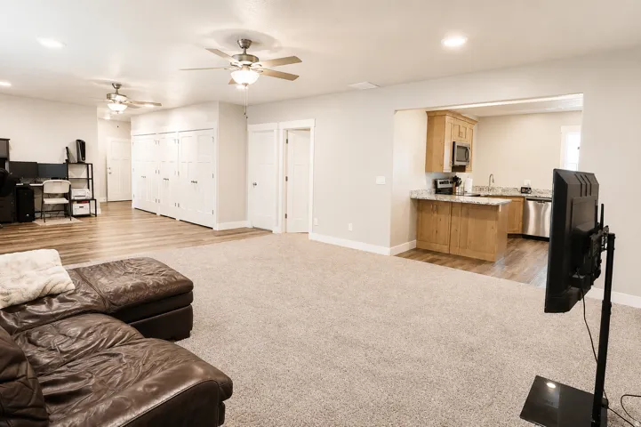 Spacious common area featuring carpet flooring, multiple ceiling fans, and an open layout to a kitchen area