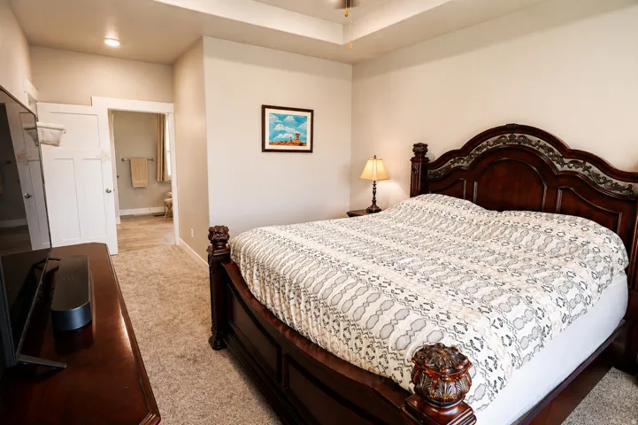 Bedroom featuring tray ceiling, recessed lighting, carpet flooring, and a doorway opening to a tiled bathroom