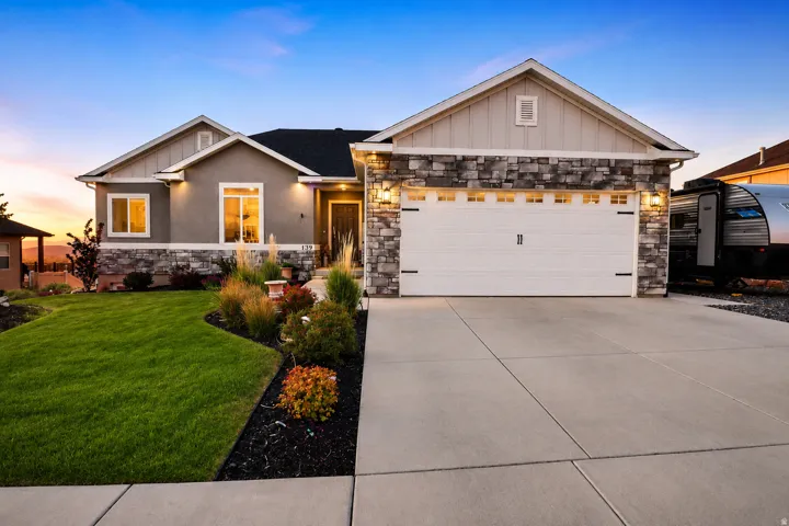 Contemporary ranch-style exterior featuring a two-car garage, stone and stucco facade, and established landscaping