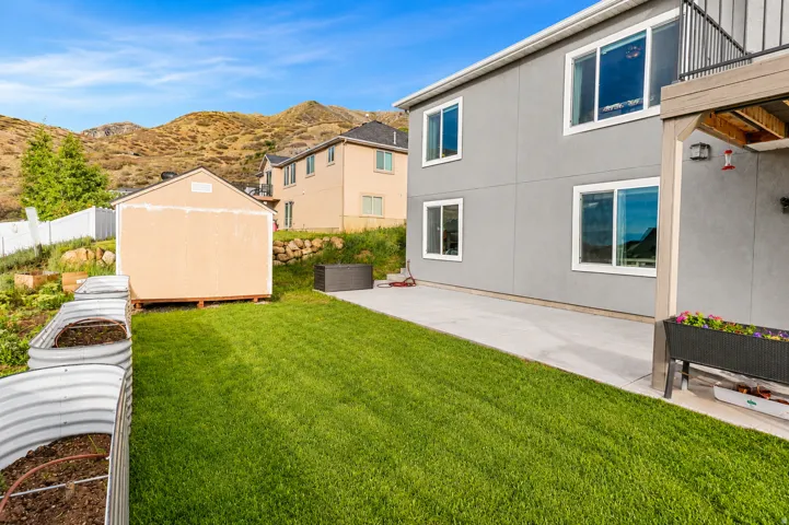 Manicured backyard featuring a concrete patio, lush green lawn, and a storage shed