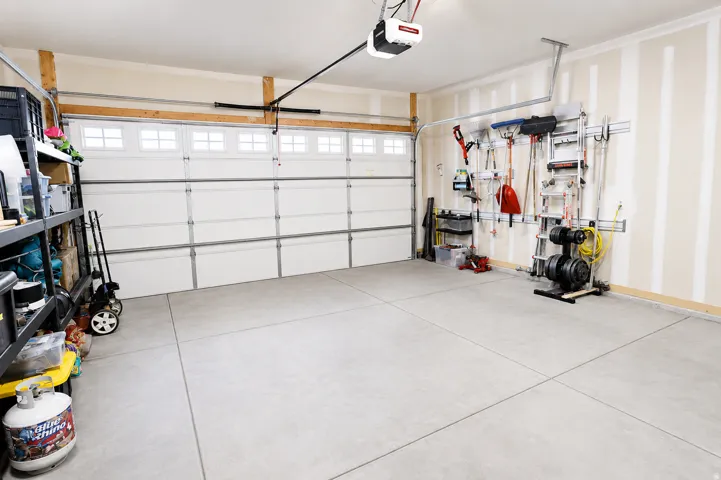 Spacious garage with a sectional overhead door featuring upper window panels, concrete flooring, and built-in wall-mounted storage tracks