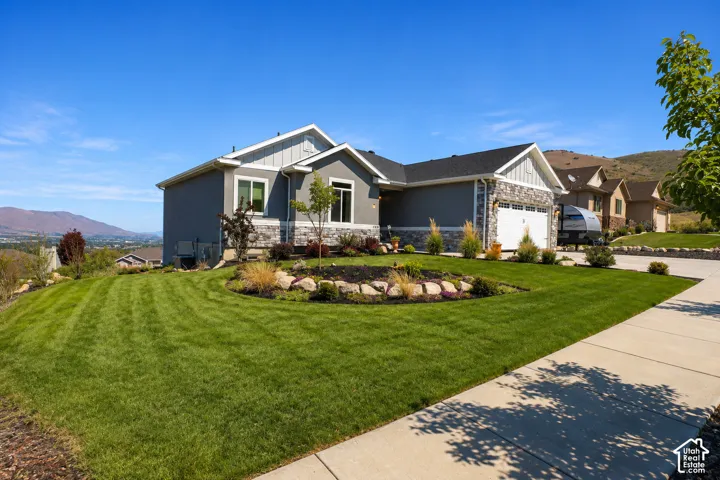 Contemporary exterior featuring a two-car garage, stone and siding accents, and a landscaped front yard with established plantings