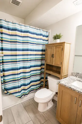 Bathroom featuring light wood-finish vanity with granite countertop, integrated sink, and chrome fixtures