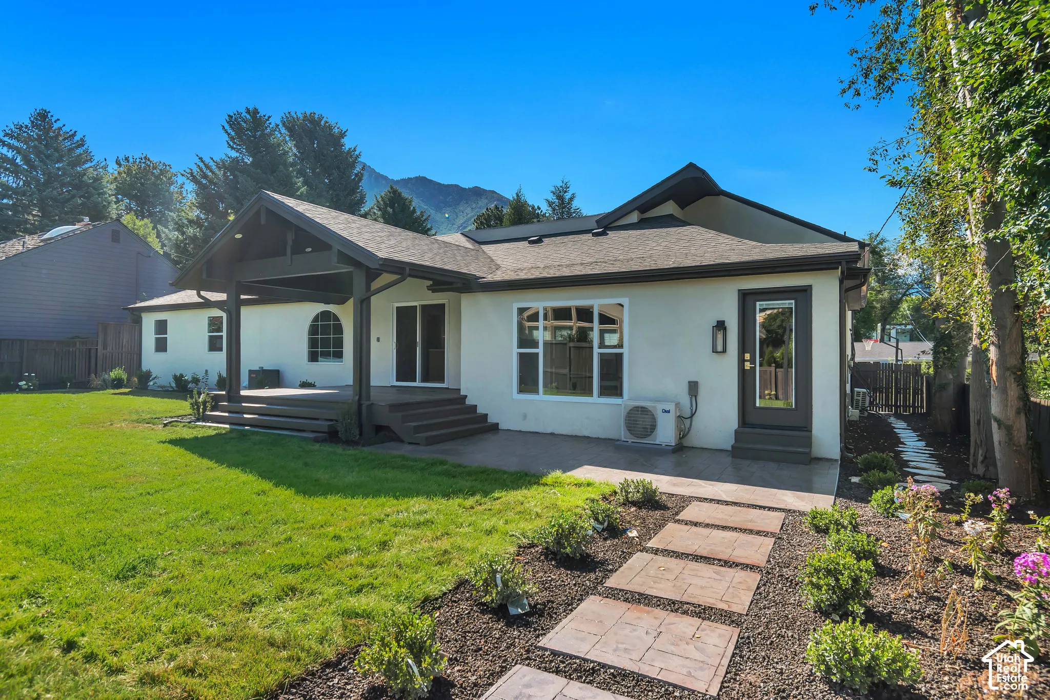 Rear exterior featuring a covered patio, expansive lawn, and mountain backdrop
