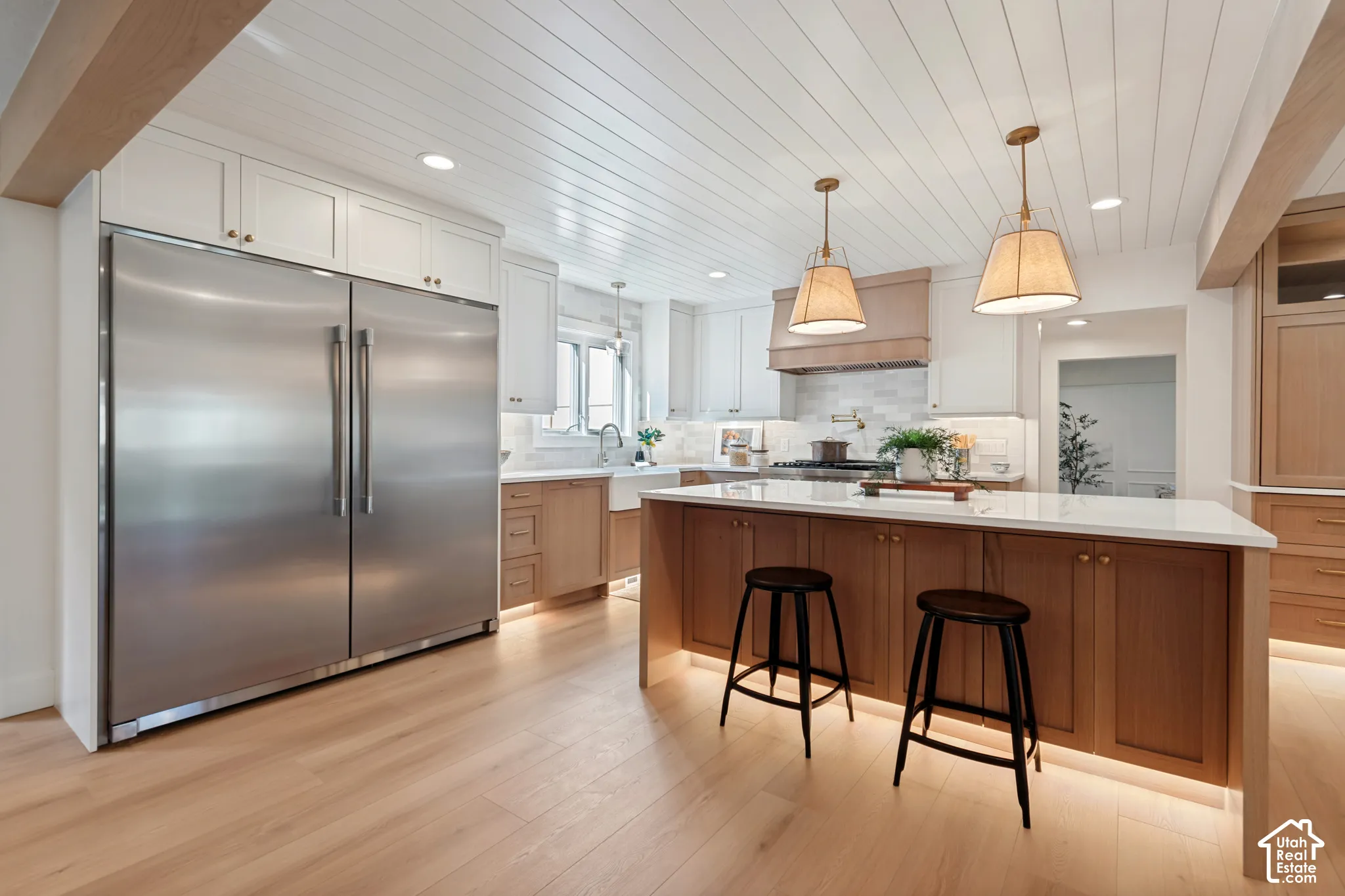 Spacious kitchen featuring an expansive center island with seating, a large stainless steel refrigerator, wood-finish flooring, white shiplap ceiling, and pendant lighting fixtures