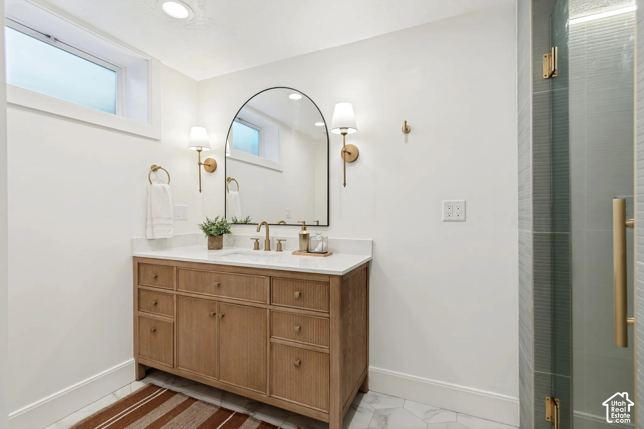 Bathroom featuring a wood vanity with a white countertop, an arched mirror, and brass sconces