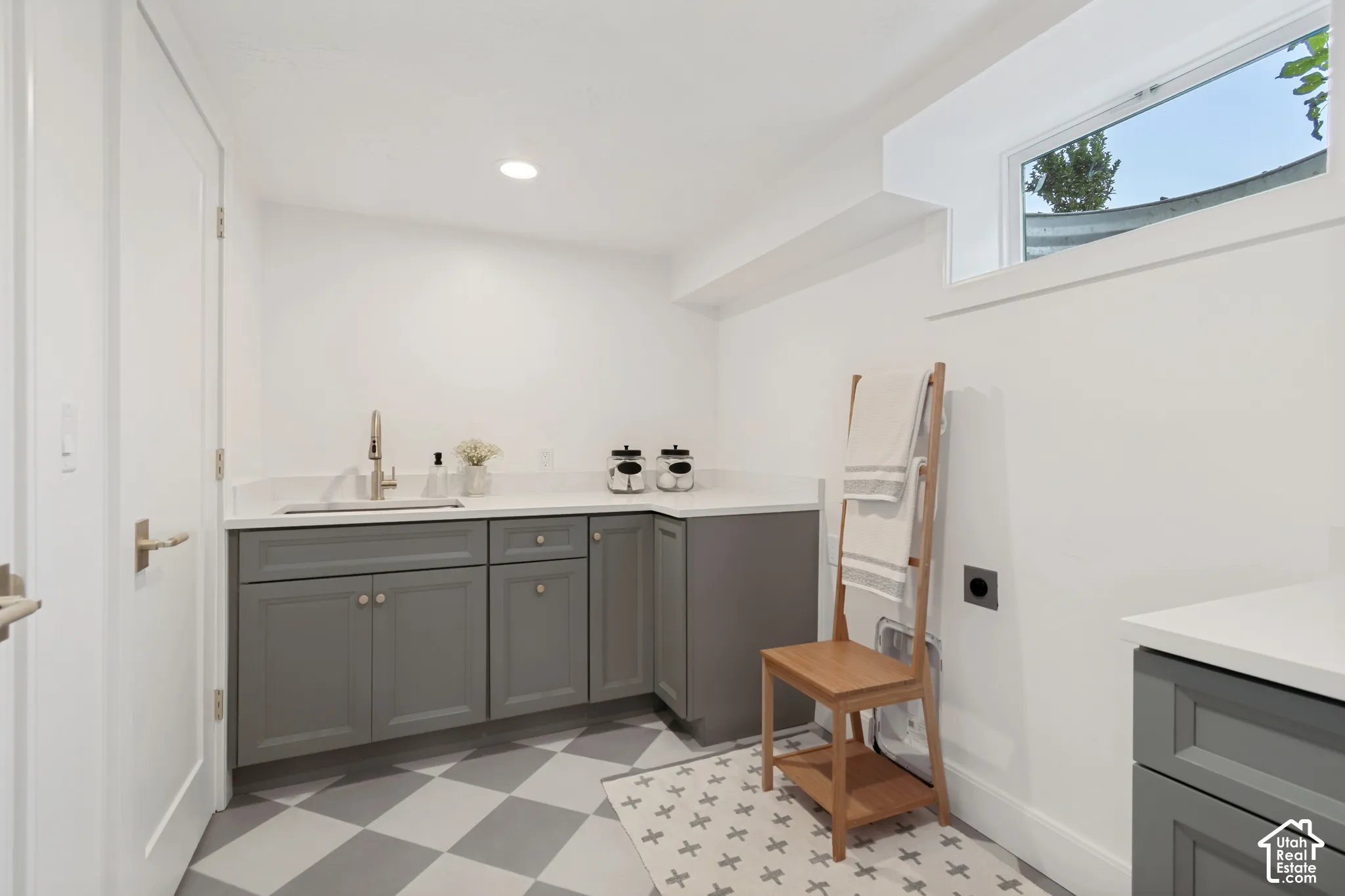 Laundry area featuring a built-in sink with a gooseneck faucet, gray cabinetry, light-toned countertops, and a checkered floor pattern