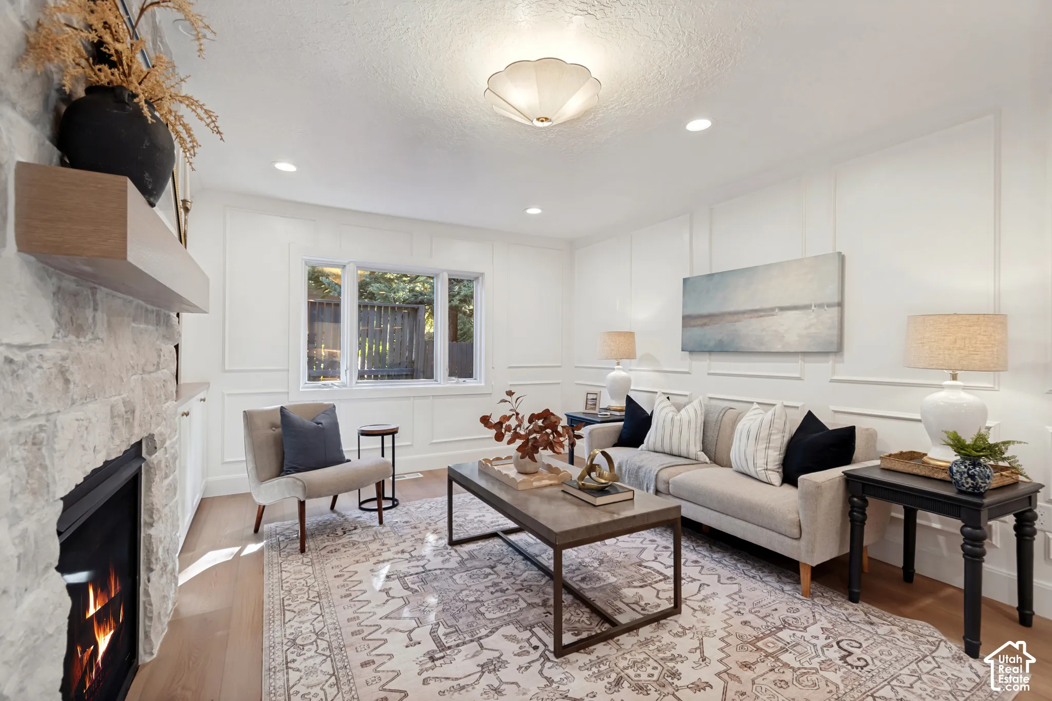 Living space featuring a stone-clad fireplace with a wood-finish mantel, wood-finish flooring, and panel molding accent walls