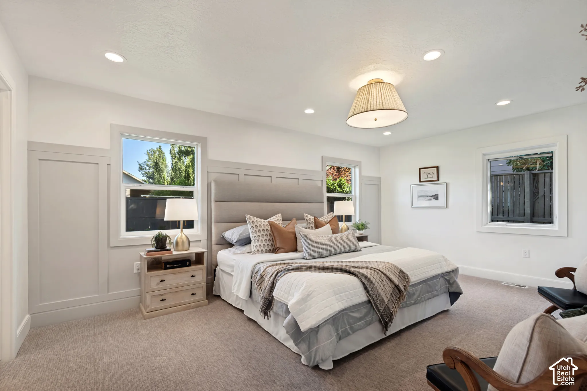 Light-filled bedroom featuring recessed lighting, a central pendant light fixture, multiple windows, plush carpeting, and wainscoting paneling