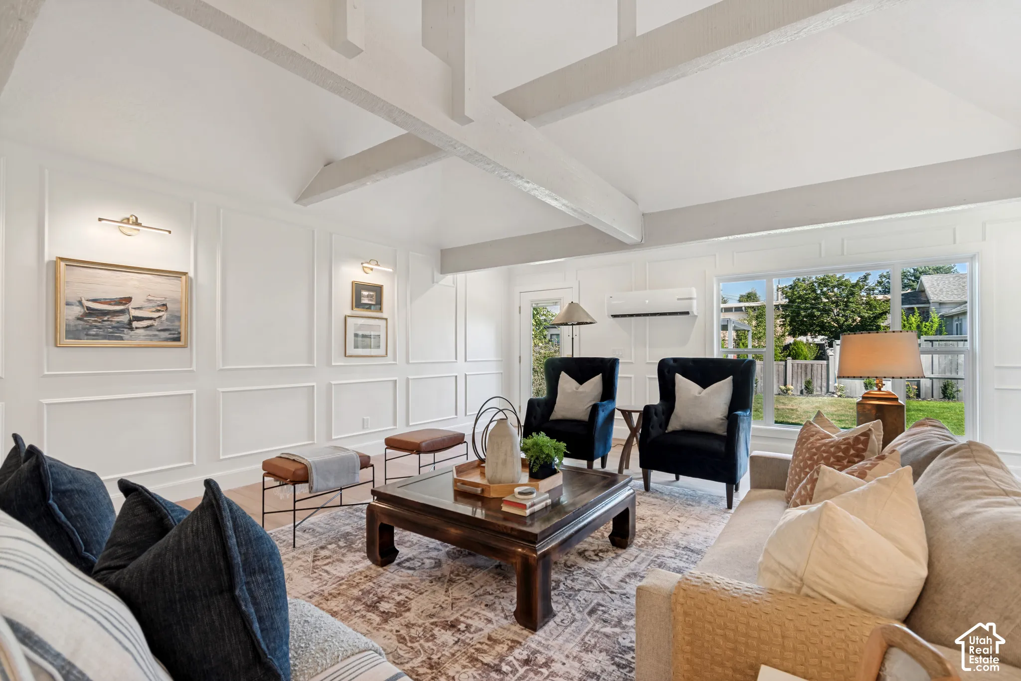 Living area featuring vaulted ceilings with exposed beams, decorative wainscoting, light wood-finish flooring, and a large window overlooking the backyard