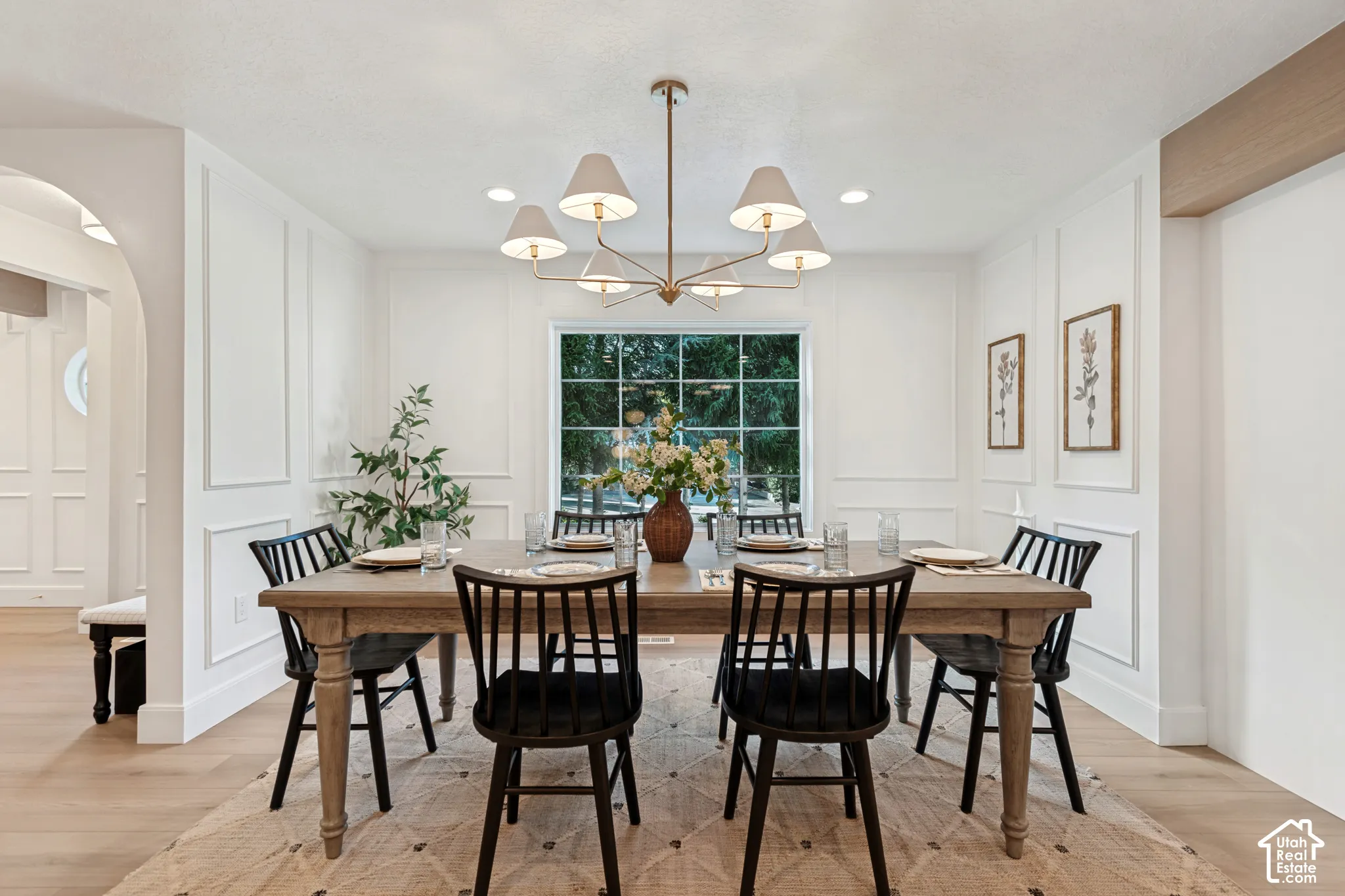 Dining area featuring wood-finish flooring, white paneled walls, a large window, and a gold-tone chandelier