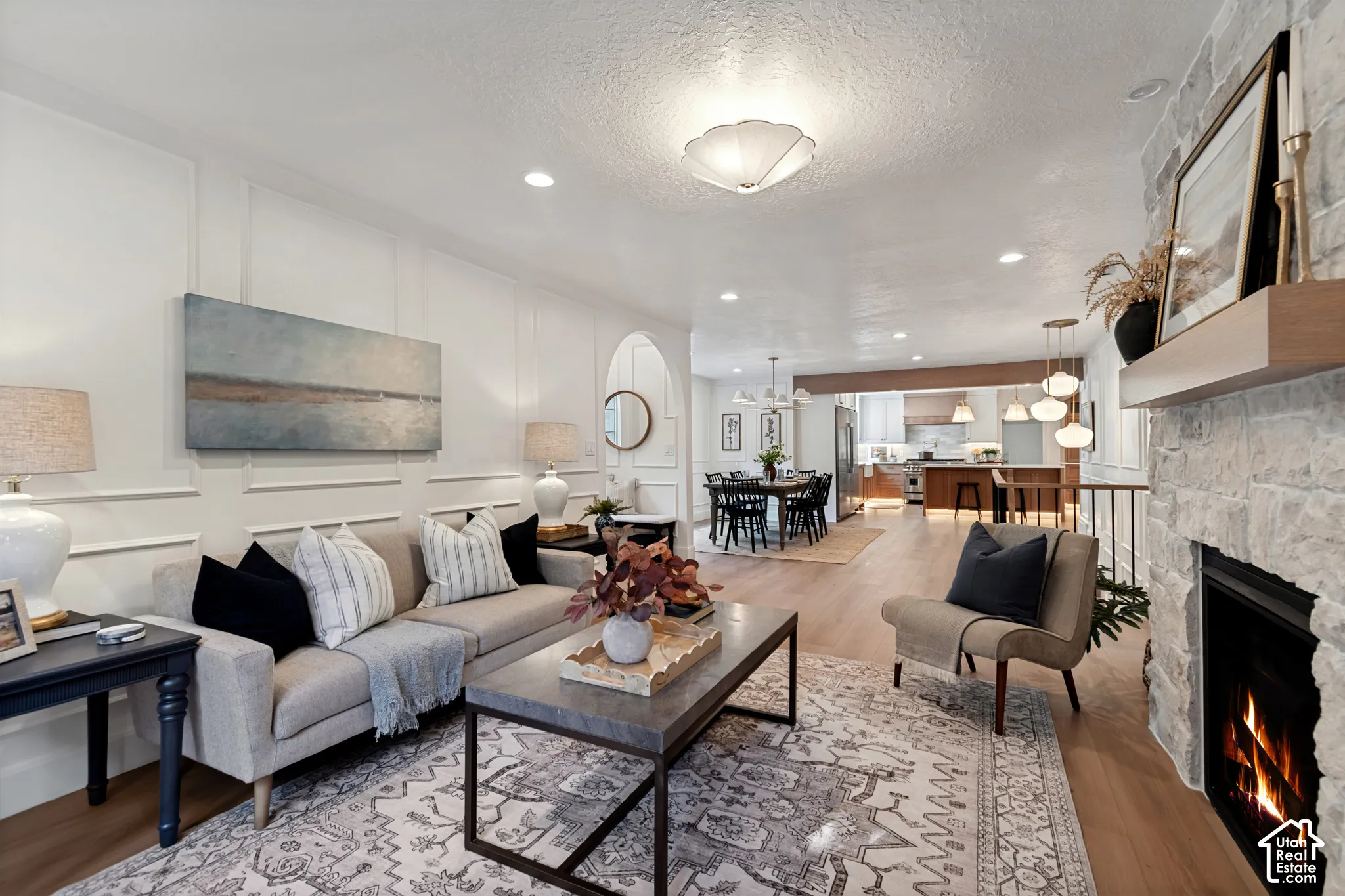 Spacious living area featuring wood-finish flooring, a stone fireplace with a wood mantel, recessed lighting, and decorative wall paneling
