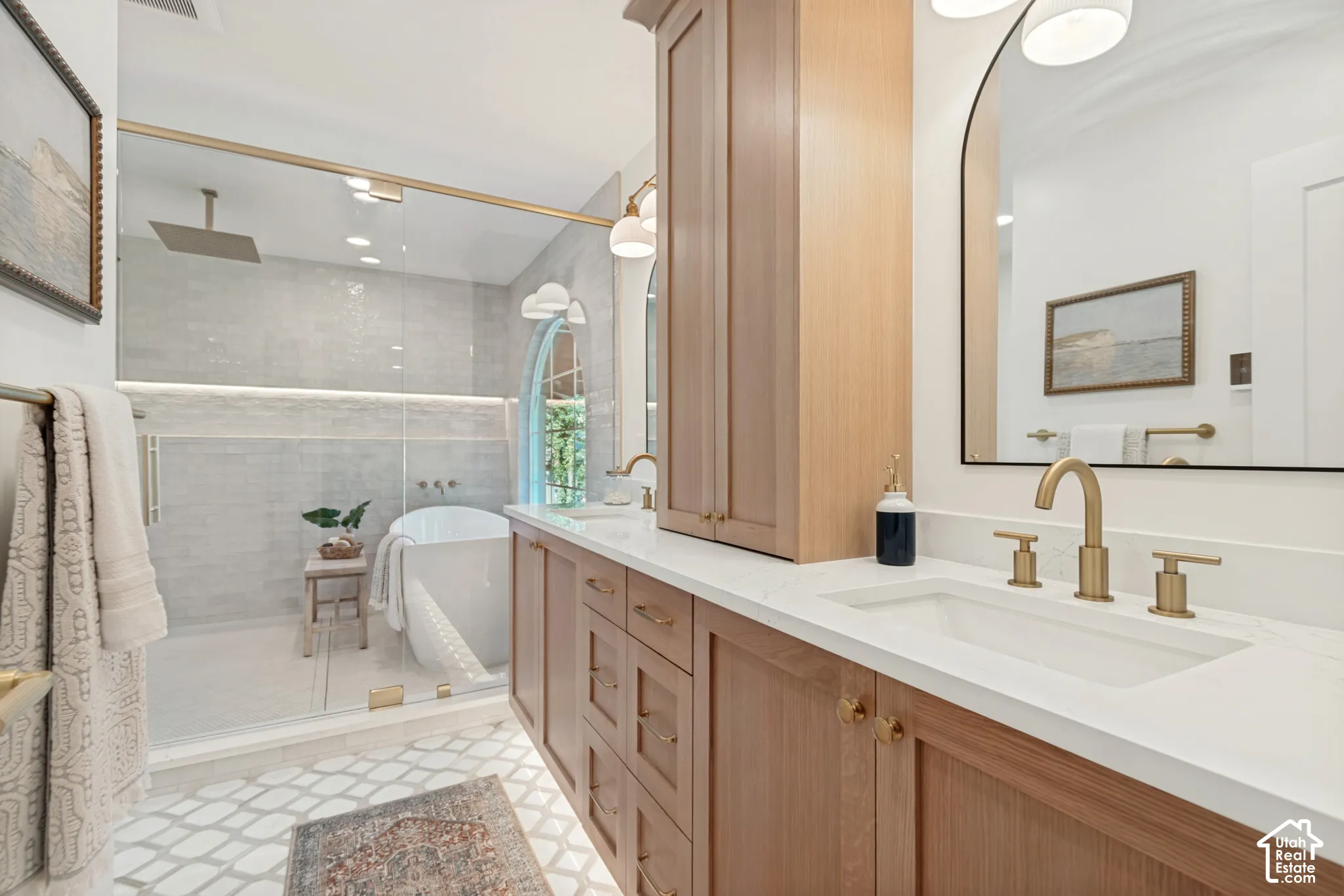 Bathroom featuring a dual vanity with light wood cabinetry, white countertops, and brass fixtures