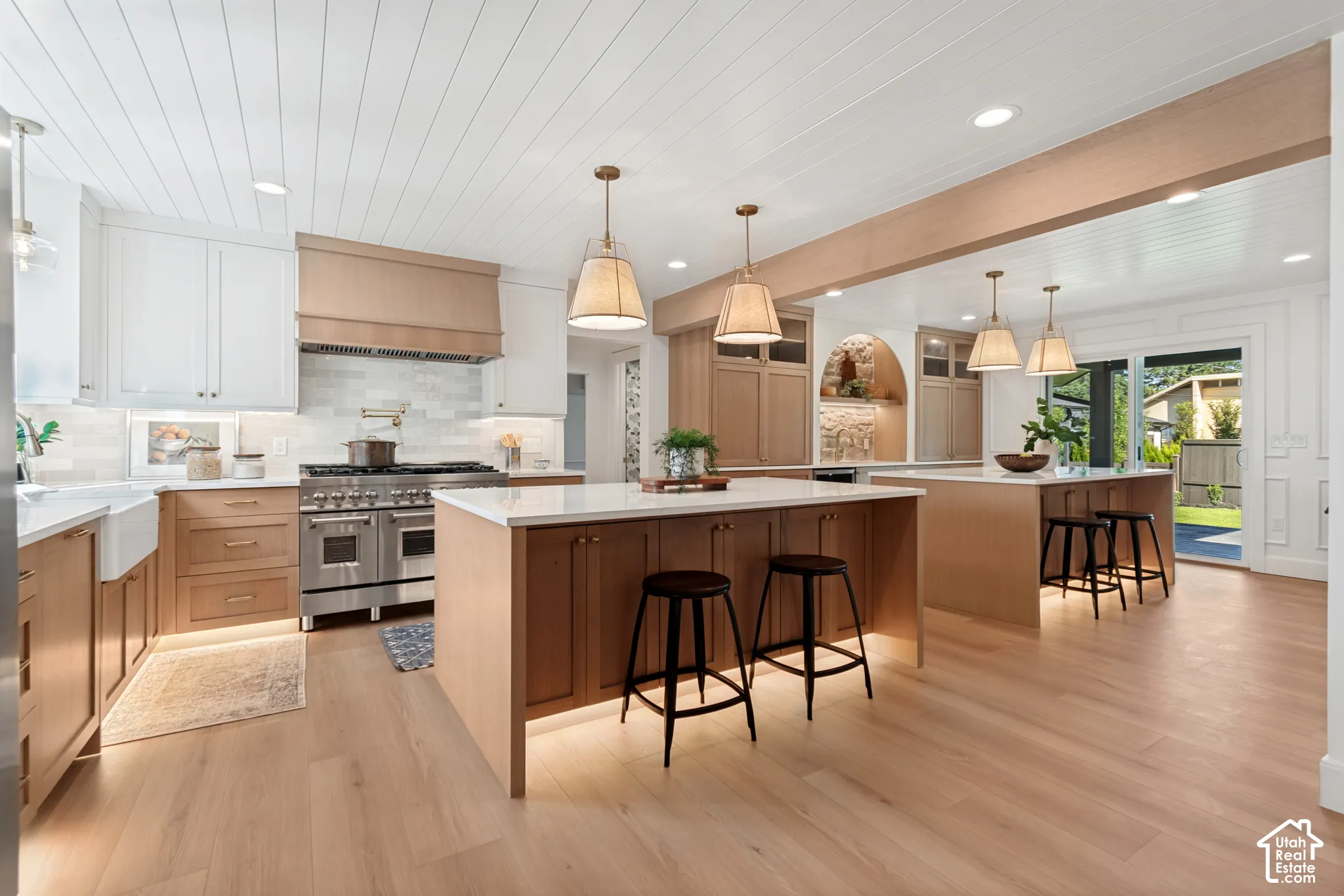 Gourmet kitchen with wood-finish flooring, two-tone cabinetry, stainless steel range, white farmhouse sink, and two kitchen islands with pendant lighting