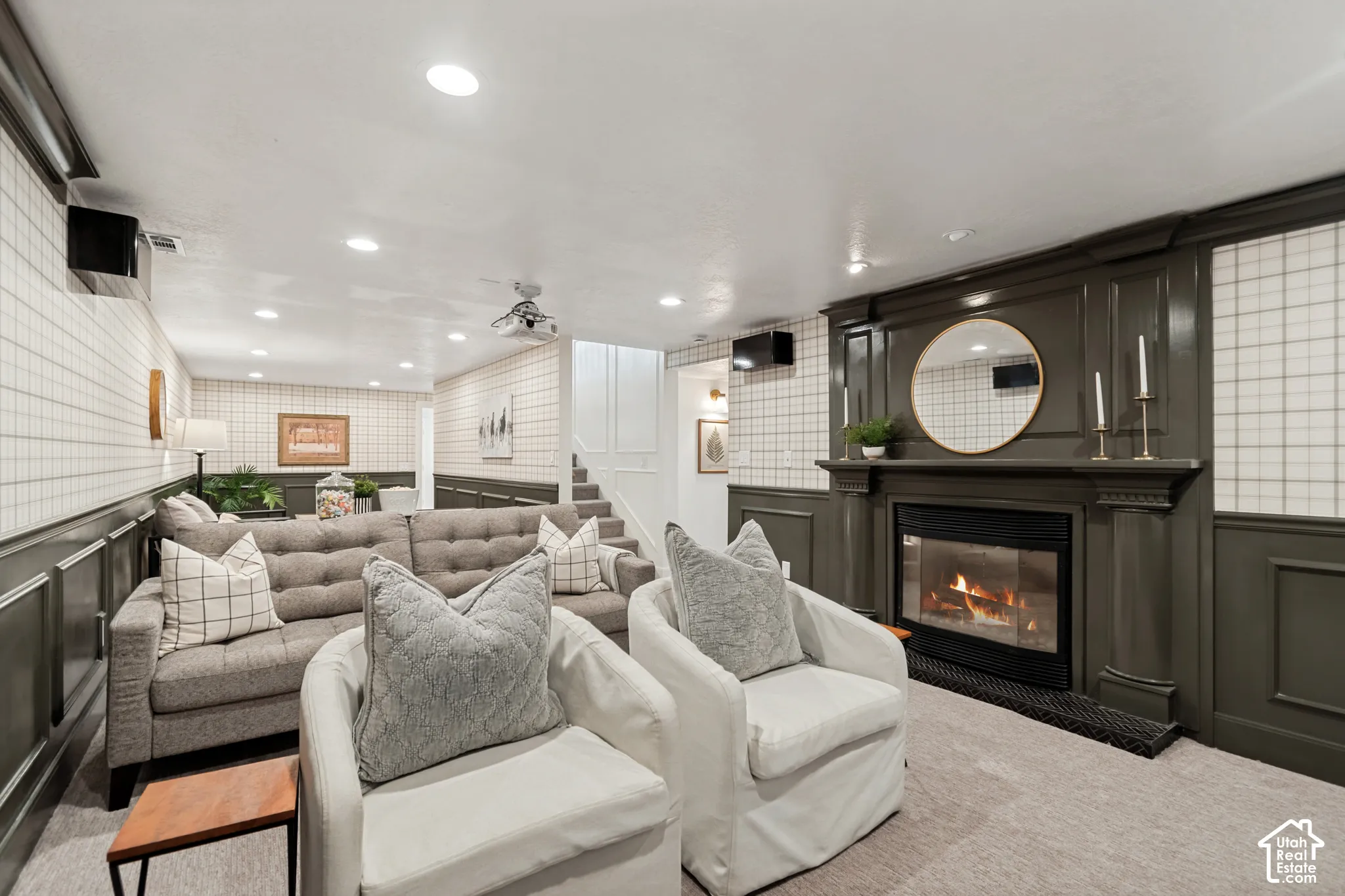 Carpeted recreation room featuring an elegant fireplace with a dark mantel, detailed wainscoting, recessed lighting, and a ceiling-mounted projector