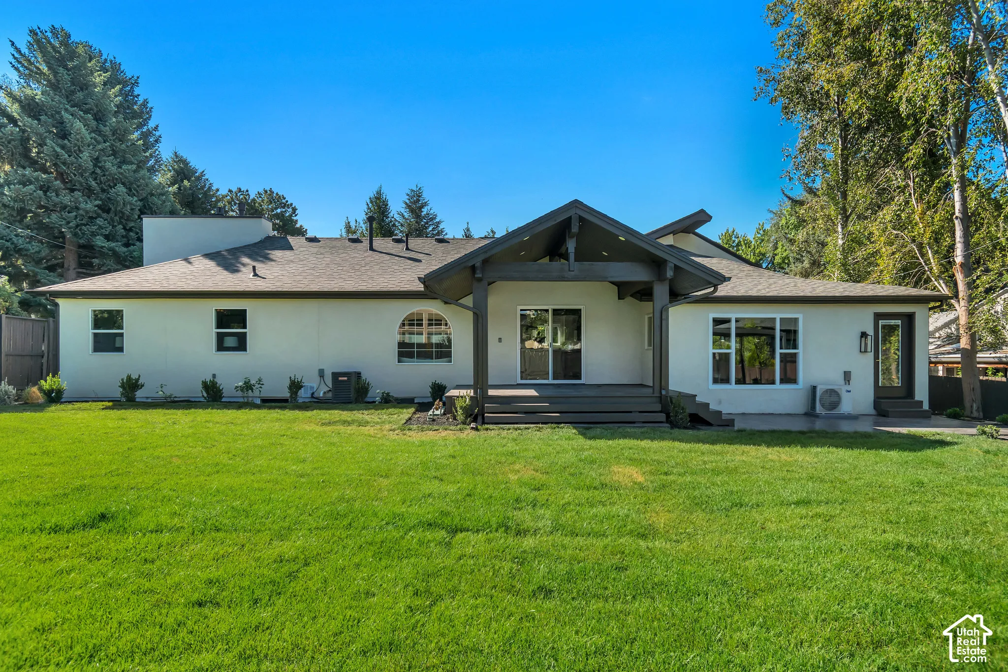 Rear exterior with a spacious green lawn, featuring an elevated deck, sliding glass doors, a covered patio area, and an arched window
